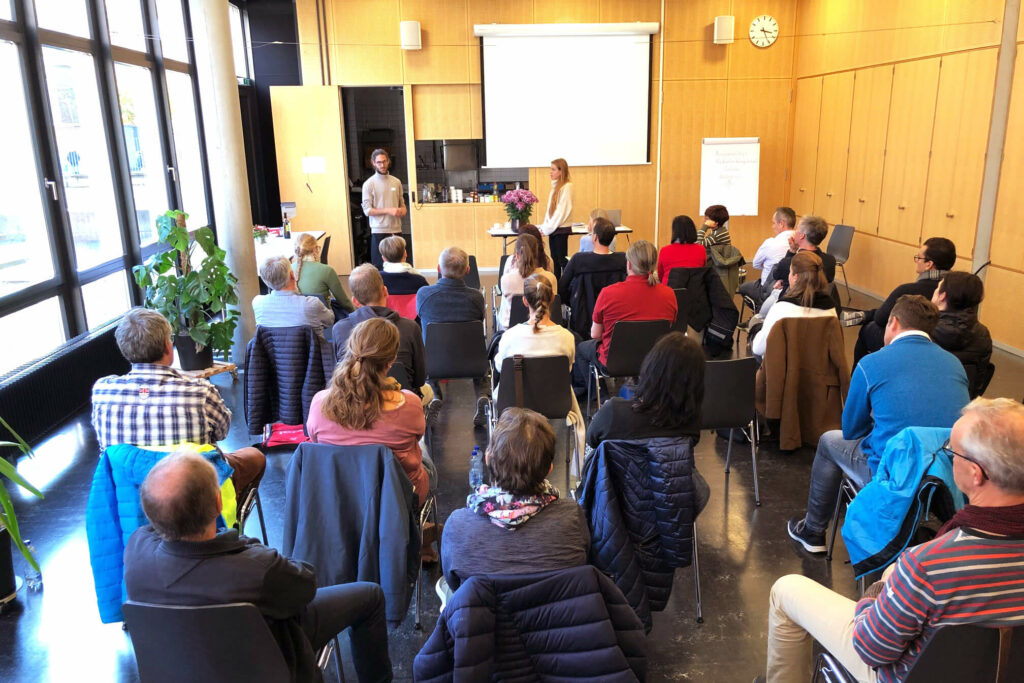 Zwei Personen leiten ein Seminar. Teilnehmende hören zu.